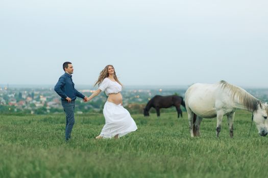 Rural couple on a green meadow communicates with animals. Pregnant wife. Therapy and relaxation for pregnant women.