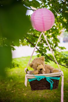 street decorations for a children's party. A basket with a teddy bear in a air balloon in a green park.