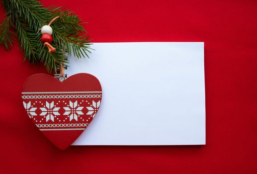Festive composition Notepad, red wooden heart with white ornament and green fir branches on a red background.Christmas and Valentine's day concept.