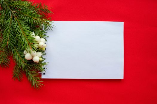 Notepad and green spruce branches with white dogwood berries on a red background. New year's Christmas concept.