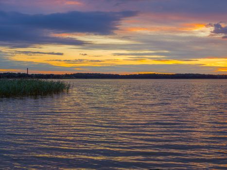 Panoramic view of evening sunset lake with green trees, mist and tranquil reflection. Estonia, Harku. Sunset over lake