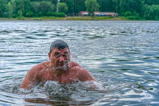 Man swims in cold water in the river against the background of the forest and the beach