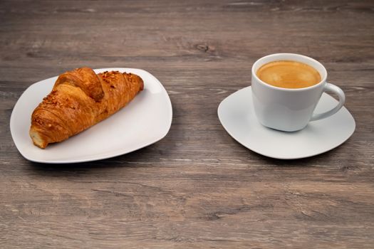 The breakfast with a delicious croissant on a plate and a coffee