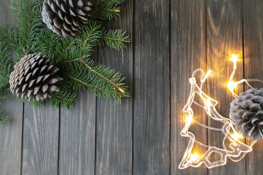 Christmas background with fir branches and big pine cones on black wooden background and lights