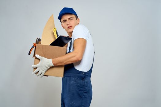 man in working uniform with a box in his hands tools loader delivery light background. High quality photo