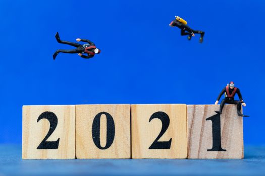 Miniature people divers diving around wooden block 2021 , Happy new Year concept