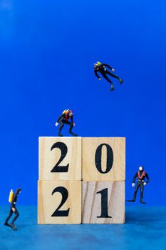 Miniature people divers diving around wooden block 2021 , Happy new Year concept