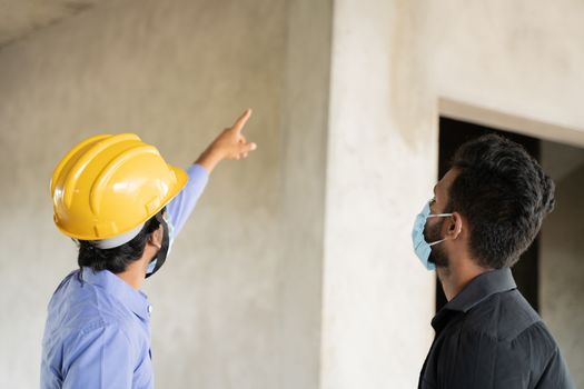 Two construction worker in medical mask busy in work while maintaining social distancing - concept of covid-19 or coronavirus safety measures at work place