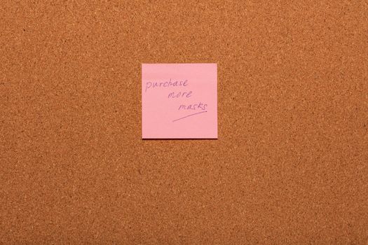 Reminder Purchase more masks handwritten on a pink sticker on a cork notice-board. Healthcare and social concepts.