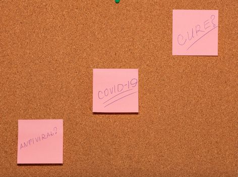 Covid-19, Antiviral?, Cure? handwritten on three pink stickers across a cork notice-board. Healthcare and social concepts.