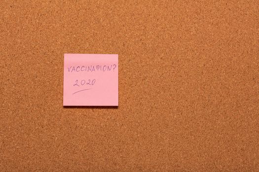 Vaccination 2020? handwritten on a pink sticker on a cork notice-board. Healthcare and social concepts.
