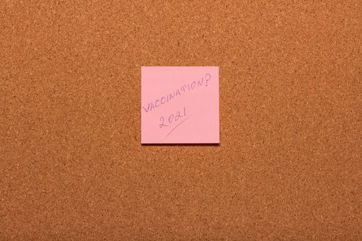 Vaccination 2021? handwritten on a pink sticker on a cork notice-board. Healthcare and social concepts.