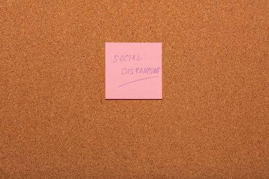 Reminder Social distancing handwritten on a pink sticker on a cork notice-board. Healthcare and social concepts.