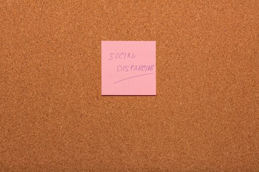 Reminder Social distancing handwritten on a pink sticker on a cork notice-board. Healthcare and social concepts.