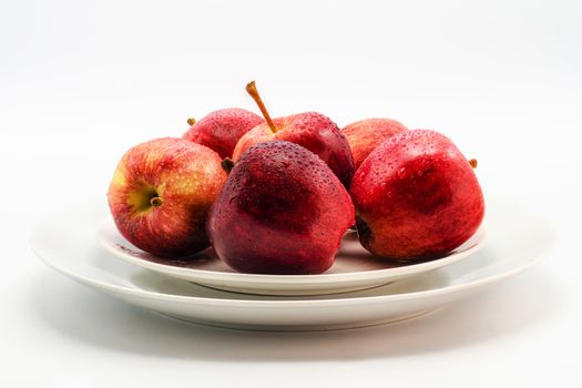 a few red apples lying on a white plate on a white background