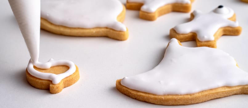 Close up of decorating cute Halloween gingerbread cookies with frosting icing cream topping bag.