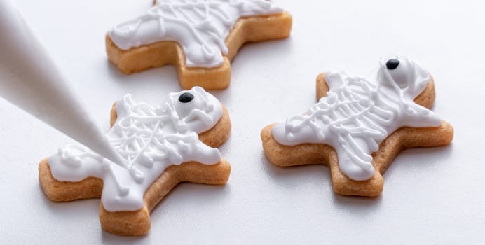 Close up of decorating cute Halloween gingerbread cookies with frosting icing cream topping bag.