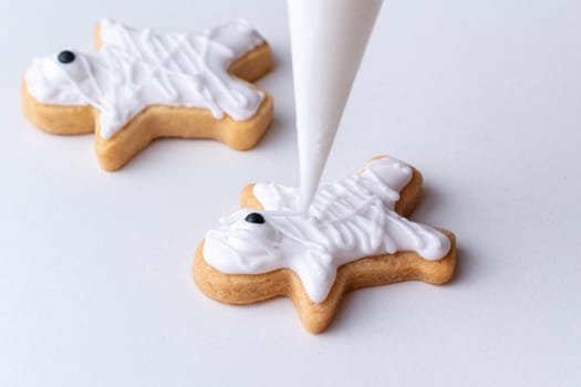 Close up of decorating cute Halloween gingerbread cookies with frosting icing cream topping bag.