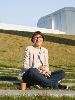 Woman sits on park bench with take away lunch box, cardboard cup of coffee. Healthy bowl with vegetables. Casual clothes, urban lifestyle of millennials. Healthy nutrition.