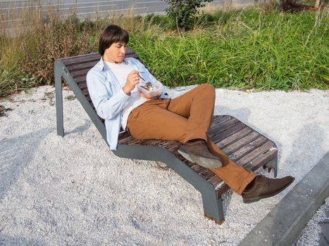 Man sits on park bench with take away lunch box. Healthy bowl with grains and meat. Casual clothes, urban lifestyle of millennials. Healthy nutrition.