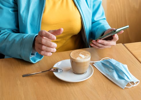 The woman removing the mask, drinking coffee and chating in the cafe during lockdown