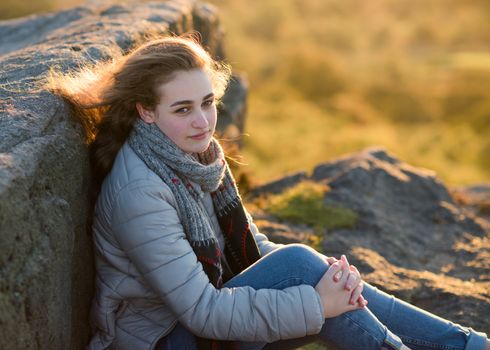 A girl sitting on top of hill against an amazing landscape in the autumn