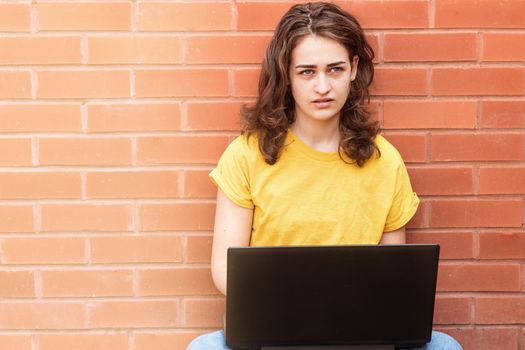 Sad young woman in yellow shirt sitting on flor, studying online and working on the laptop