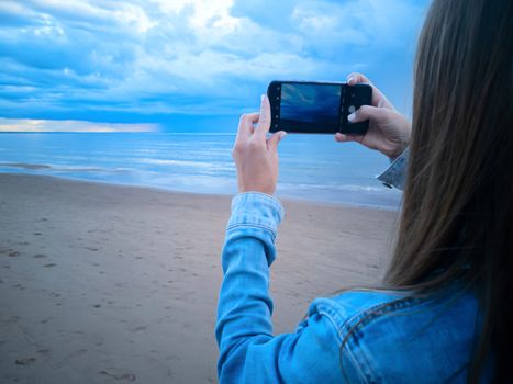 beautiful alone girl on the beach. Girl looking at stormy sea and taking a picture with smarphone. The spectacular Storm with rain Is Coming in Estonia. Baltic sea