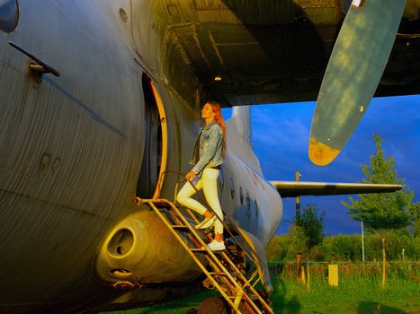 Yo ungwoman standing at plane ladder going to board, outdoors, airport. Old Soviet military airplane, sunset time. Close up of a Abandoned Historic Aircraft. Close up of propeller engine.