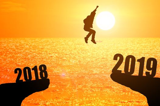 Silhouette of young man jumping between 2018 and 2019 years with beautiful sunset at the sea-concepts of news year and business target.