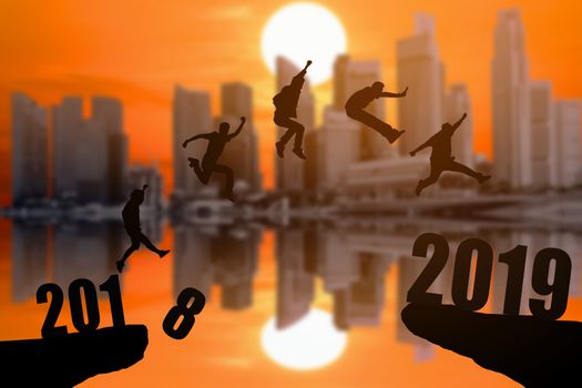 Silhouette group of young mans jumping between 2018 and 2019 years with beautiful sunset at the skyscrapers background, concepts of news year and business target.