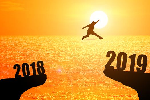 Silhouette of young man jumping between 2018 and 2019 years with beautiful sunset at the sea-concepts of news year and business target.
