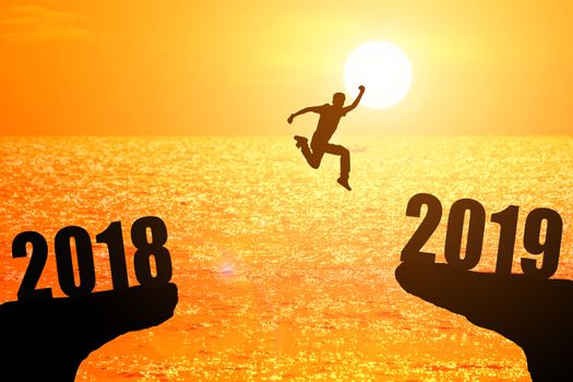 Silhouette of young man jumping between 2018 and 2019 years with beautiful sunset at the sea-concepts of news year and business target.