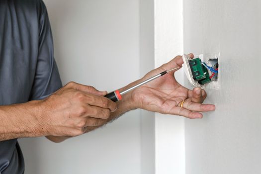 The electrician is using a screwdriver to attach the power cord to the wall outlet.