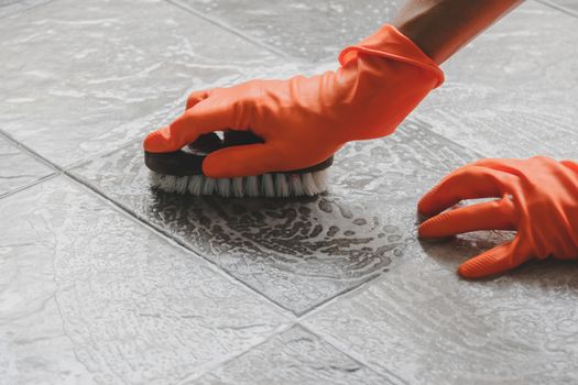 Hand of man wearing orange rubber gloves is use a hose to clean the tile floor.