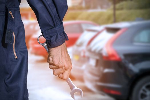 Car repairman wearing a dark blue uniform standing and holding a wrench that is an essential tool for a mechanic and has a backdrop as a car repair center, Automotive industry and garage concepts