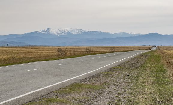 autumn paved road with passing cars on the background of snow capped mountains in the Northern cold territories
