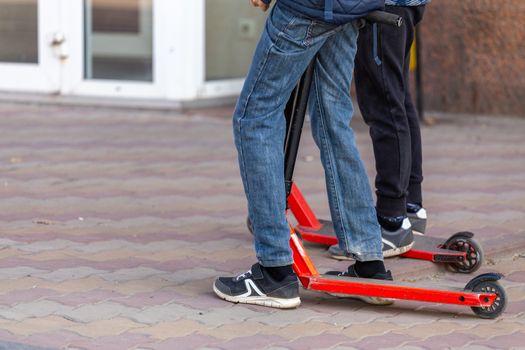 slim kids legs with scooters on the urban pavement sidewalk - closeup witn selective focus.