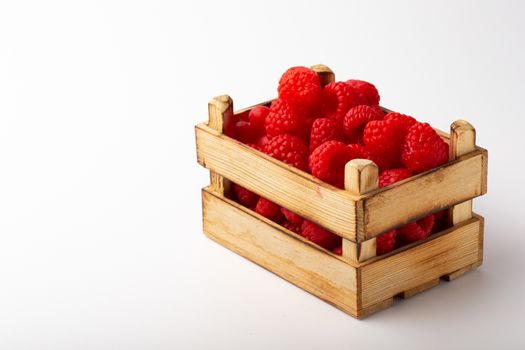 Some raspberries in a small wooden box on a white background