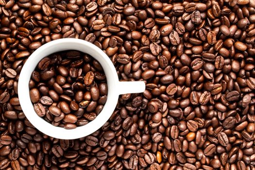 A White cup with coffee beans on a background of coffee beans