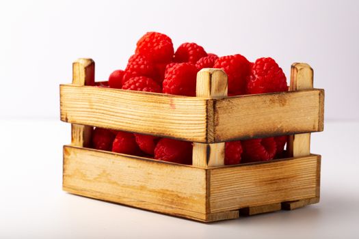 Some raspberries in a small wooden box on a white background