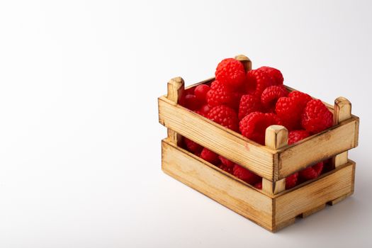Some raspberries in a small wooden box on a white background