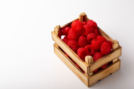 Some raspberries in a small wooden box on a white background