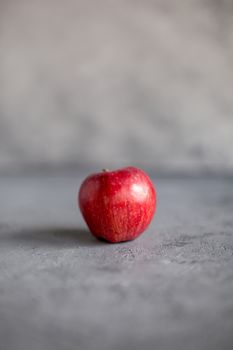one Ripe garden red apples on gray concrete. Fruits concept of the fall harvest. Space for text. Selective soft focus.