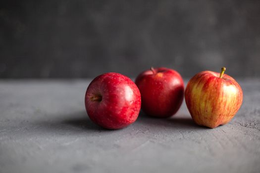 Three Ripe garden red apples on gray concrete. Fruits concept of the fall harvest. Space for text. Selective soft focus.