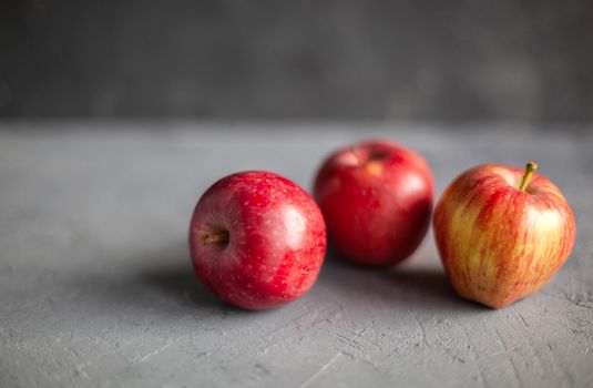 Three Ripe garden red apples on gray concrete. Fruits concept of the fall harvest. Space for text. Selective soft focus.