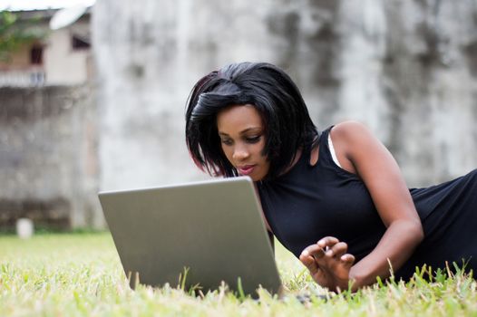 young woman lying on the lawn is focused on her laptop.