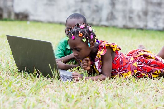 two children lying in the garden use a laptop