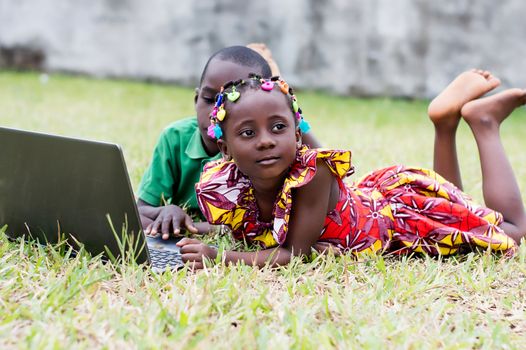 Happy children using a laptop lying in the garden