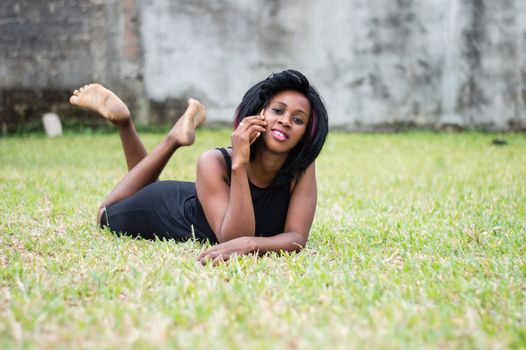 young woman in black dress is lying in the garden talking on the phone